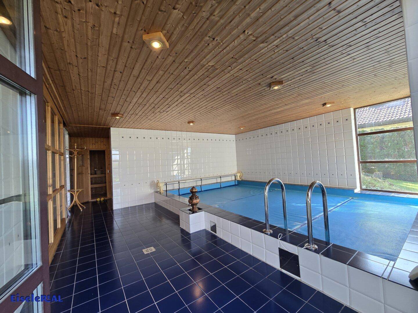 Großzügiger Innenpoolbereich mit Holzdecke, Fliesenboden und großen Fenstern.