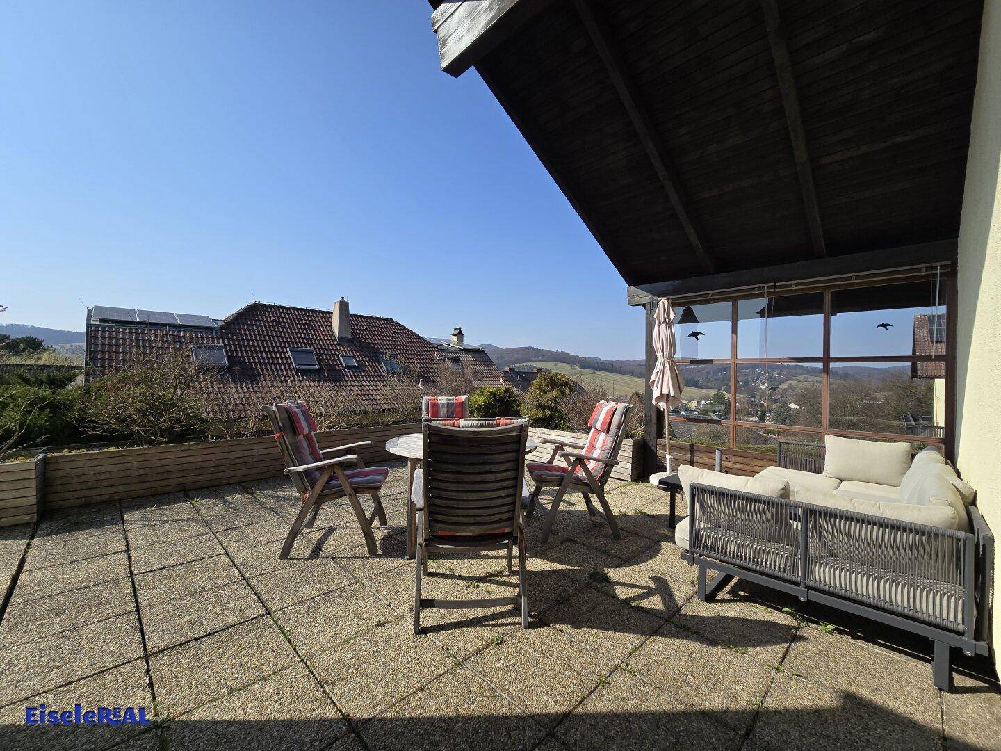 Große gepflasterte Terrasse mit Gartenmöbeln und weitem Blick über die Landschaft.
