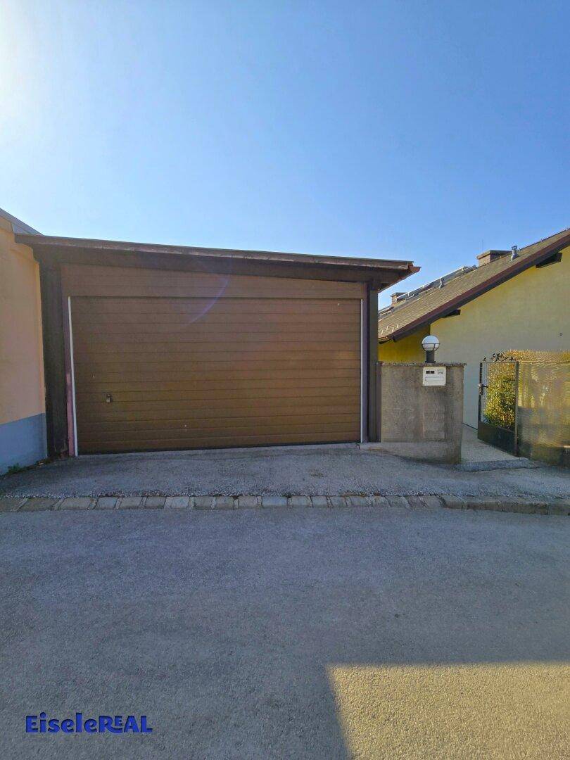 Geschlossene Garage mit braunem Tor und Zufahrt auf dem Grundstück.