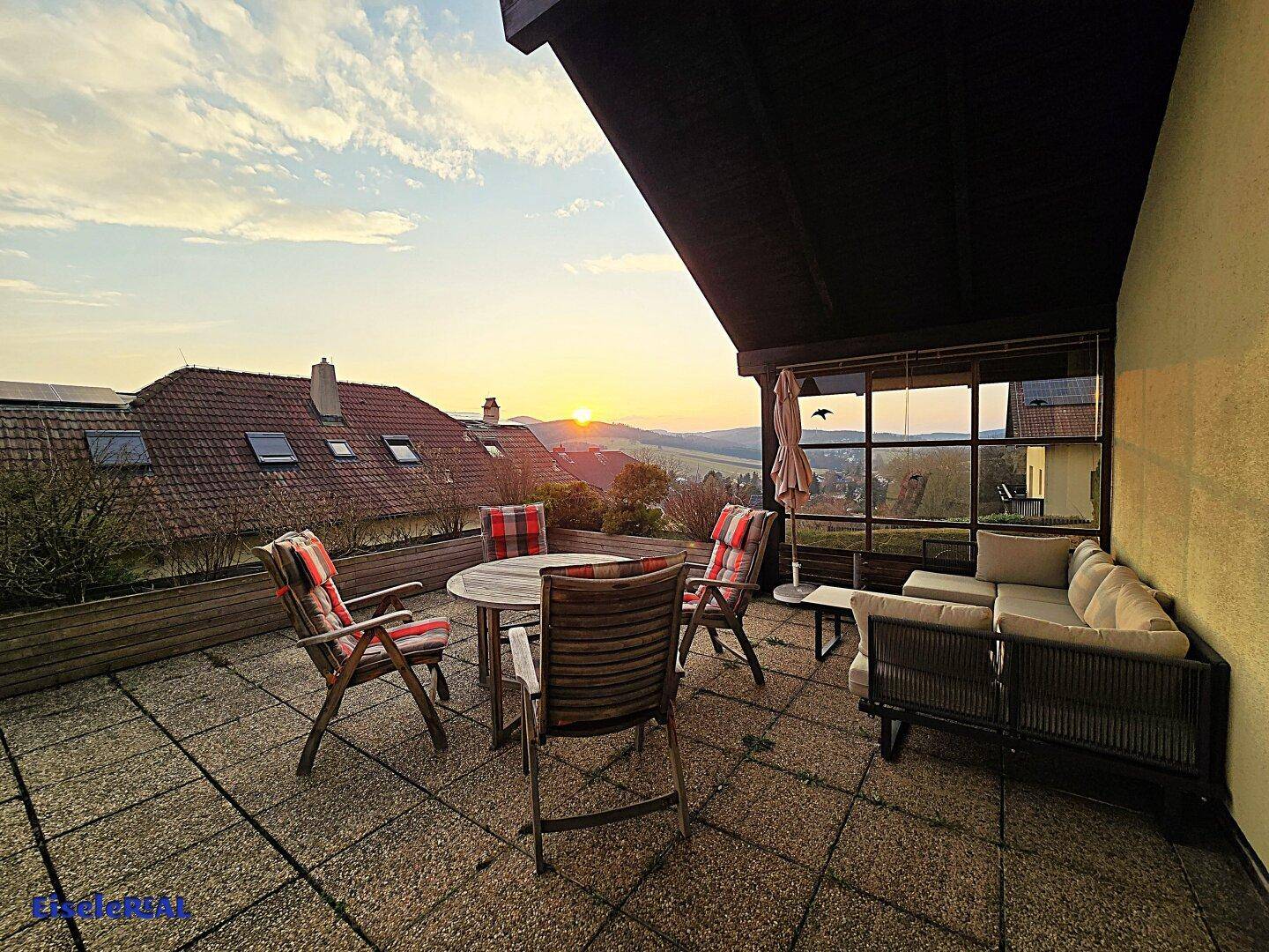 Sonnenterrasse mit Sitzgelegenheiten und malerischem Sonnenuntergang über der Landschaft.