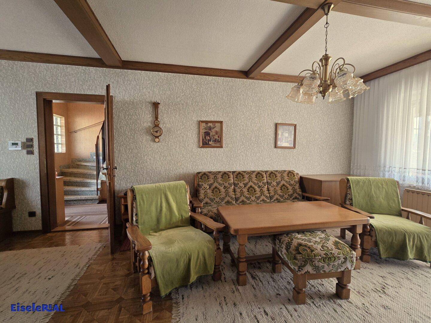 Wohnzimmer mit traditionellen Möbeln, gemusterter Tapete und Holzbalkendecke.