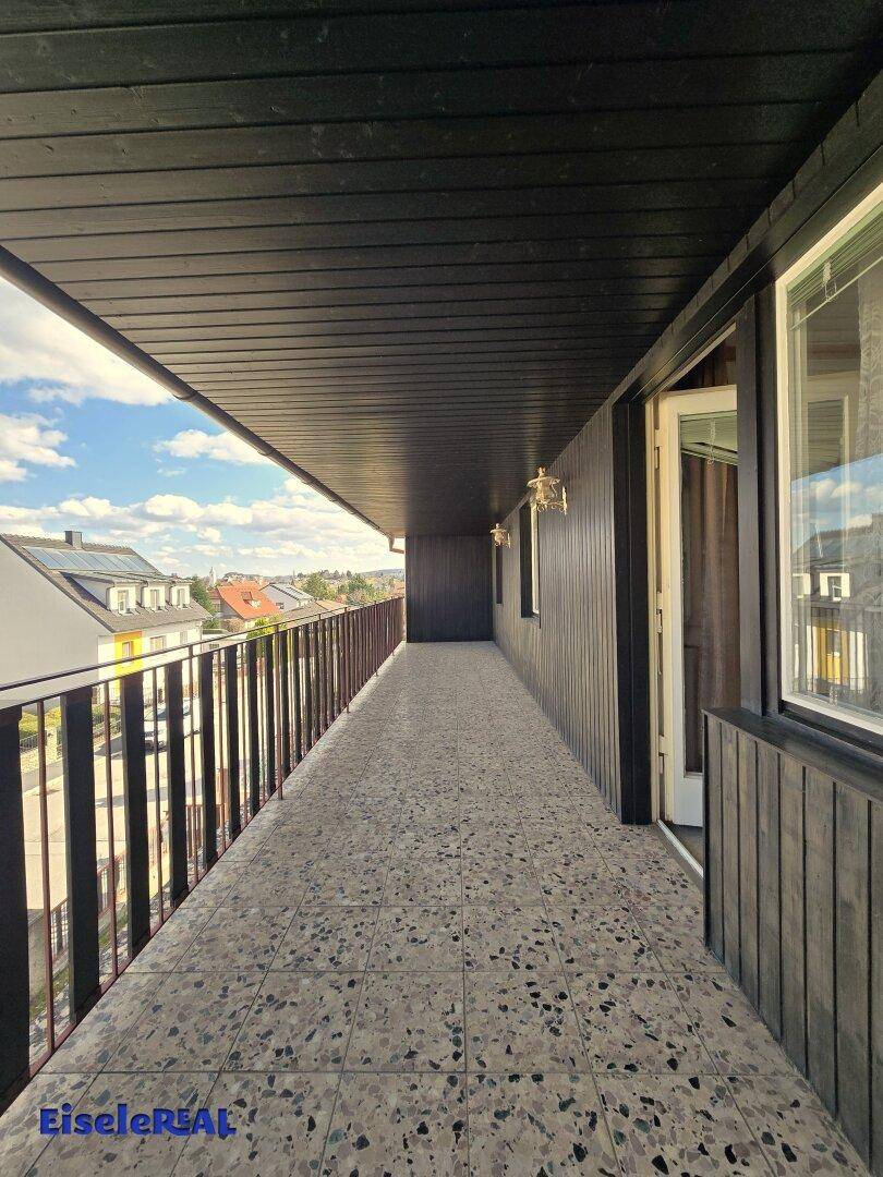 Langer, überdachter Balkon mit Fliesenboden und weitem Blick über die Umgebung.