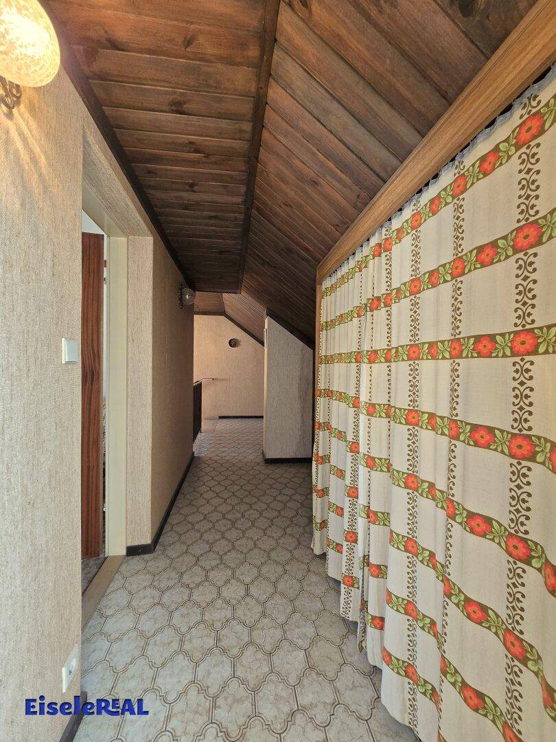 Flur im Dachgeschoss mit Holzdecke, gemusterter Tapete und Teppichboden.