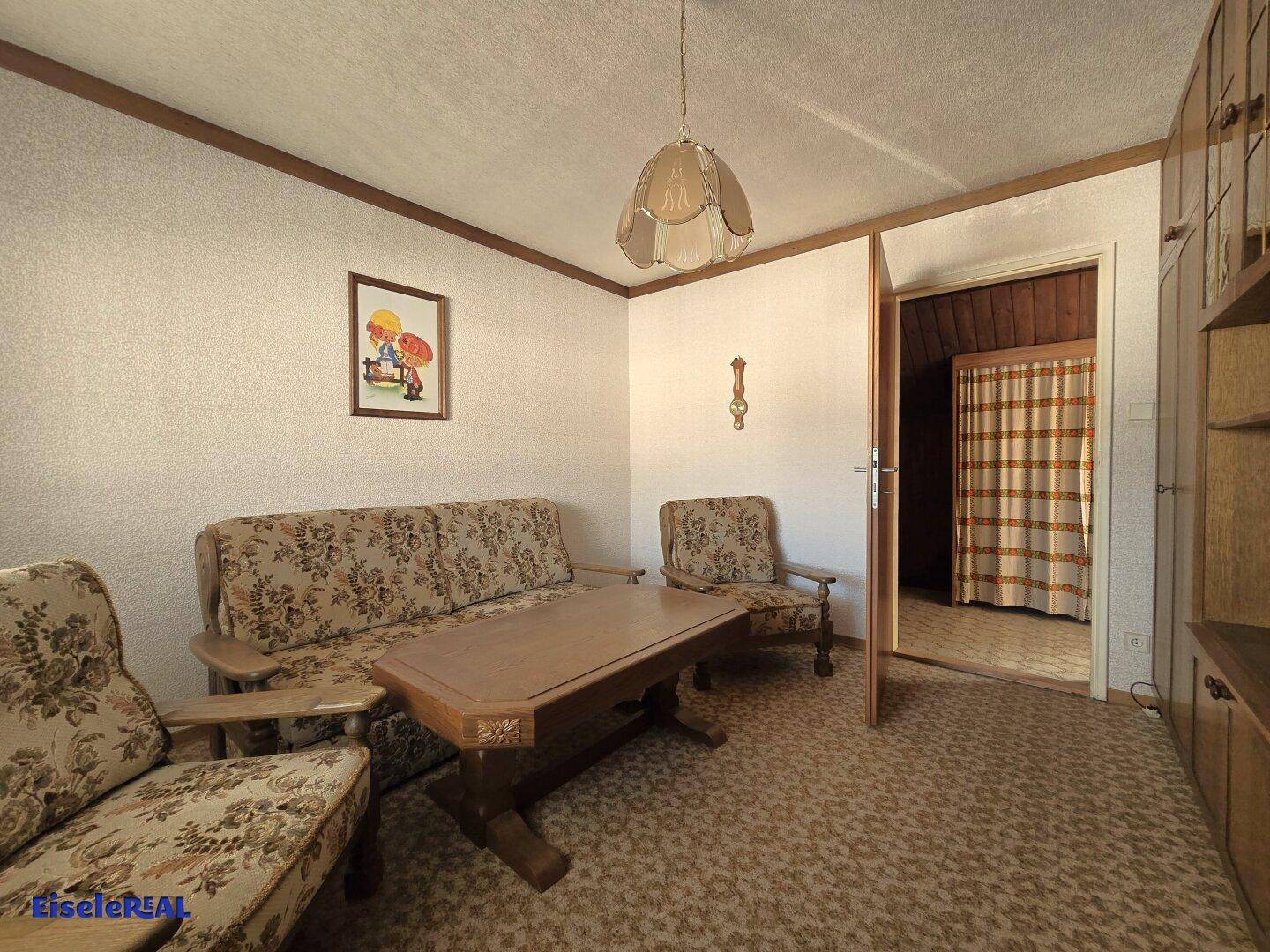 Wohnzimmer mit traditionellen Möbeln, gemusterter Tapete und Teppichboden.