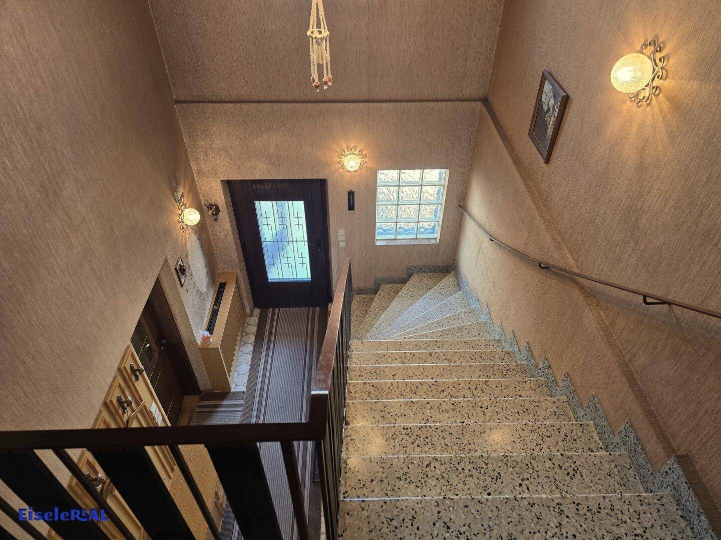 Treppenhaus mit Terrazzostufen, Holzgeländer und natürlichem Lichteinfall.