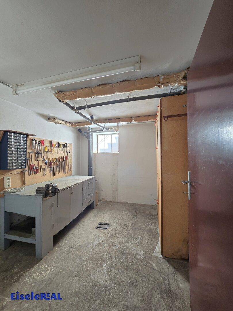 Werkstattraum im Keller mit Werkbank, Werkzeugen und Fenster.