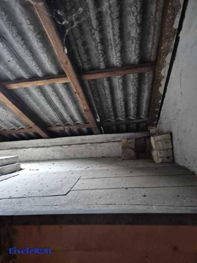 Unfertiger Dachbodenbereich mit sichtbaren Holzbalken und Wellplattenverkleidung, bereit für Ausbau.