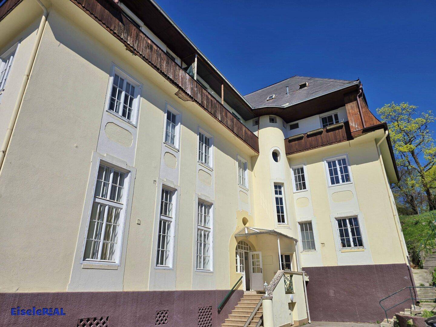 Historisches Gebäude mit gelber Fassade, Eingangsbereich und Mansarddach.