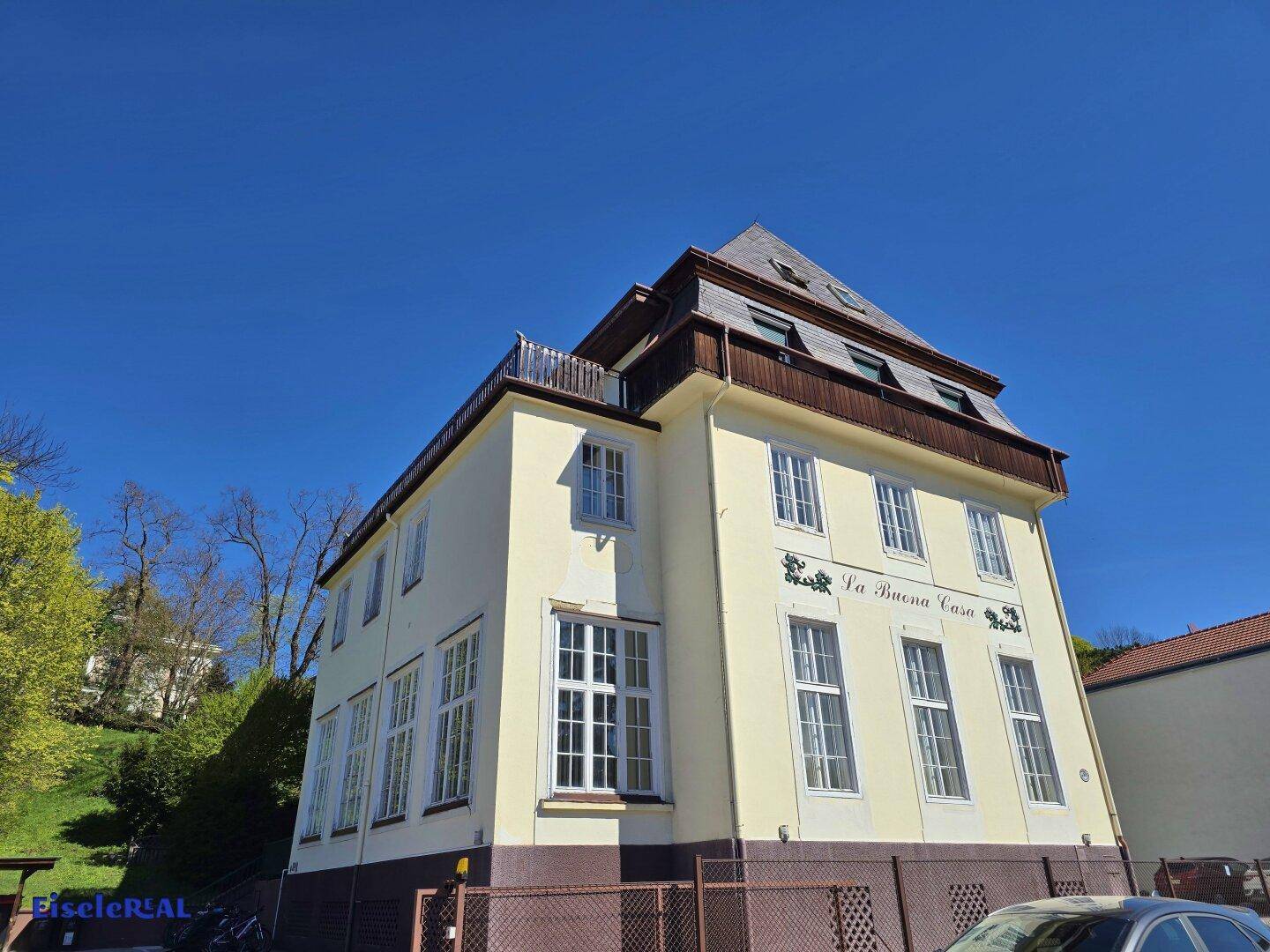 Historisches Gebäude mit gelber Fassade, Mansarddach und dekorativer Schrift.