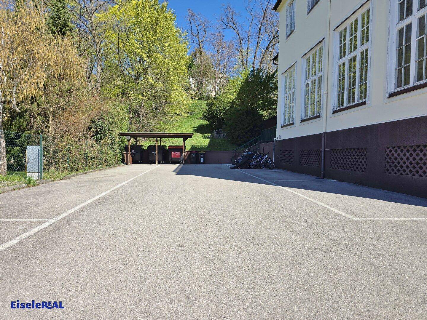 Außenparkplatz mit überdachtem Unterstand und Fahrrädern im Grünen.