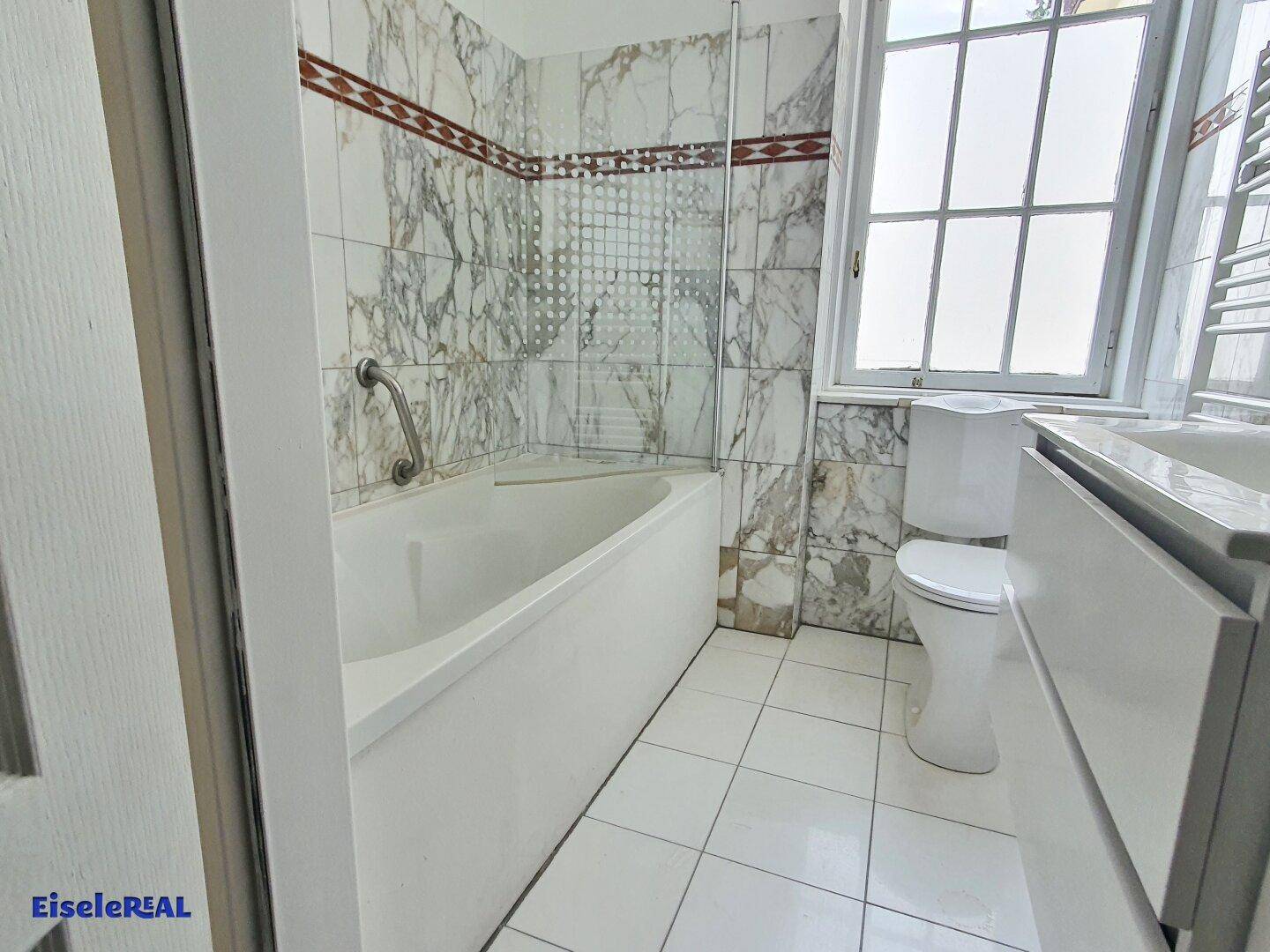 Badezimmer mit Badewanne, Marmorfliesen und Fenster für Tageslicht.