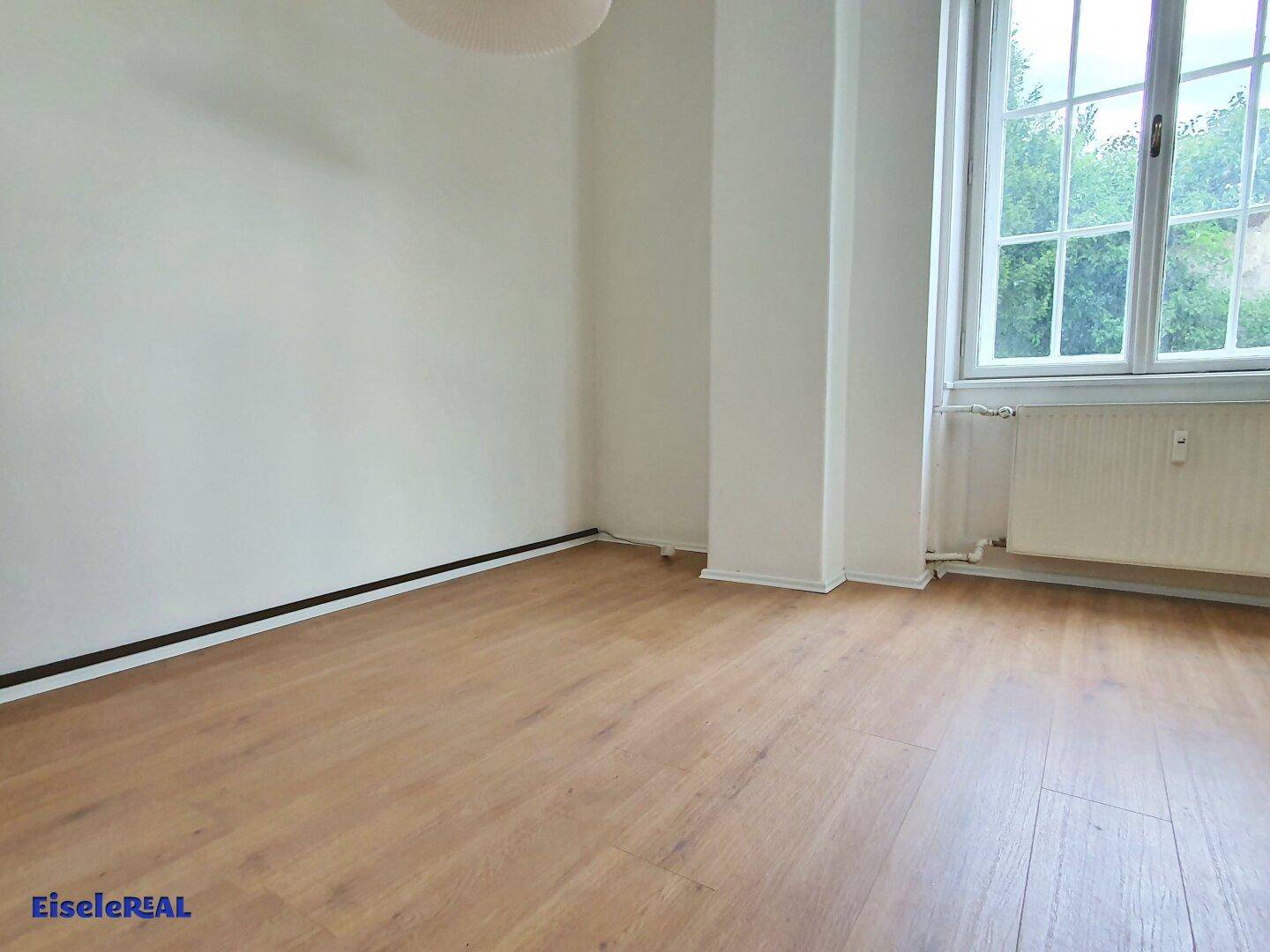 Helles Zimmer mit Holzboden und großem Fenster, das viel Licht spendet.