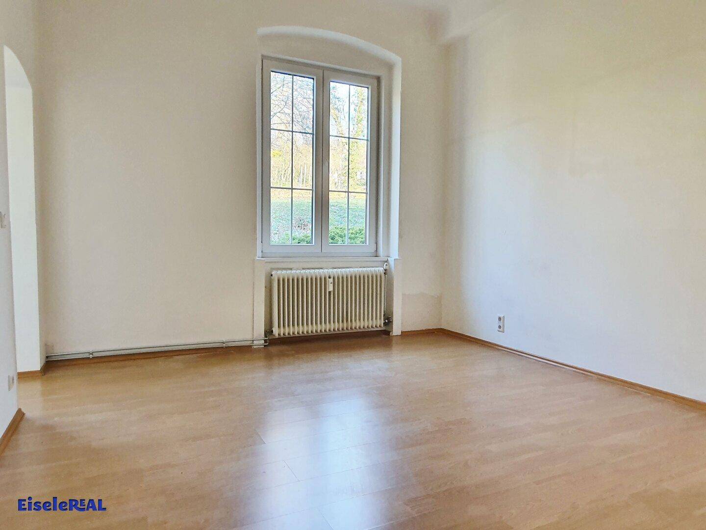 Helles Zimmer mit Holzboden und großem Fenster, das viel Licht spendet.
