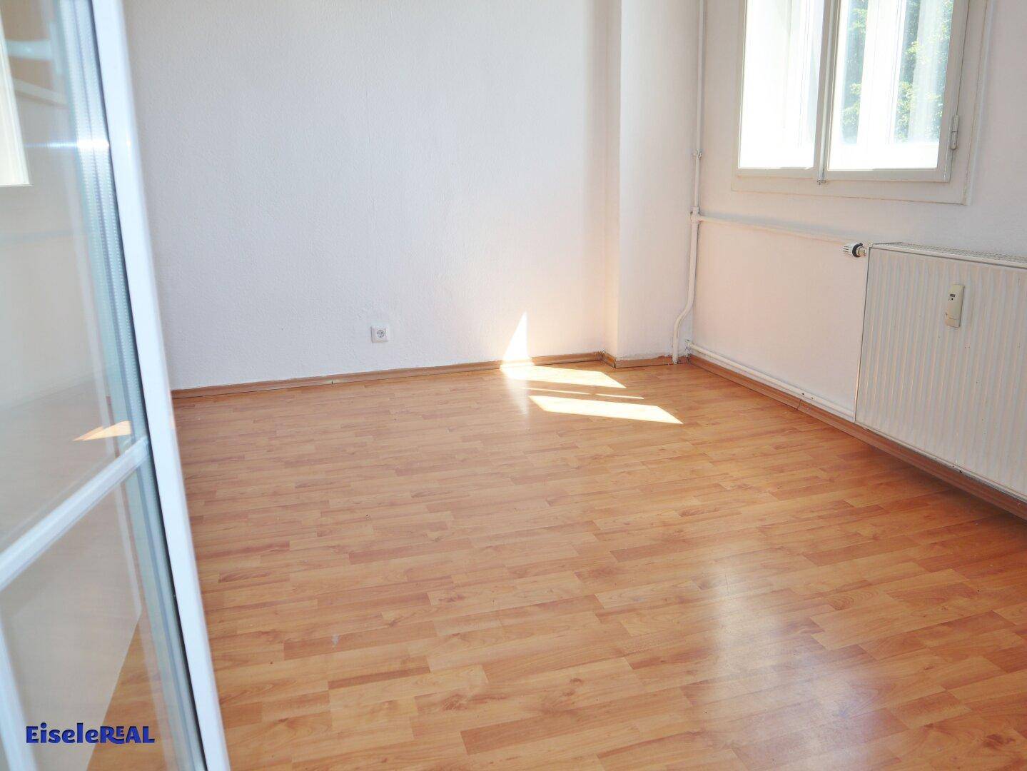 Helles Zimmer mit Laminatboden und Fenster, das viel Tageslicht hereinlässt.