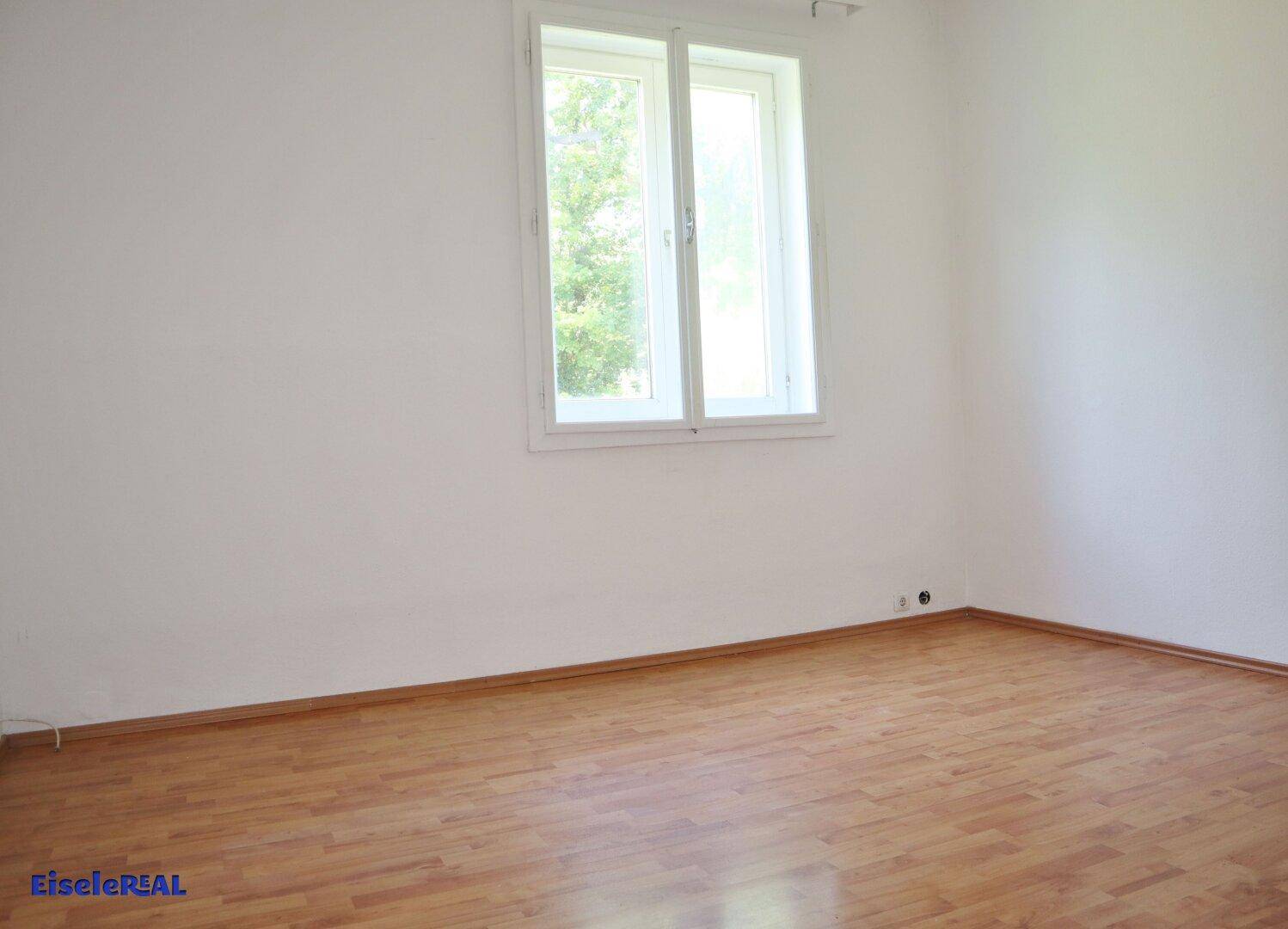 Helles Zimmer mit Laminatboden und Fenster, das viel Tageslicht hereinlässt.