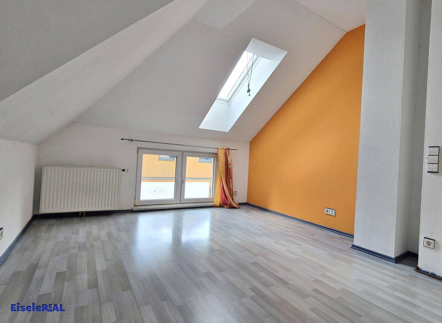 Geräumiges Zimmer im Dachgeschoss mit schrägen Wänden, Laminatboden und einem Dachfenster.