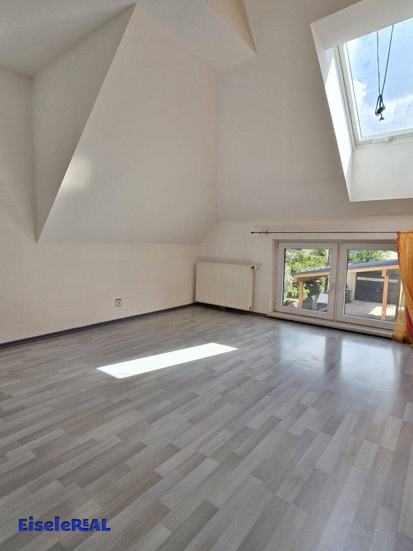 Helles Dachzimmer mit schrägen Wänden, grauem Laminatboden und einem Dachfenster für viel Licht.