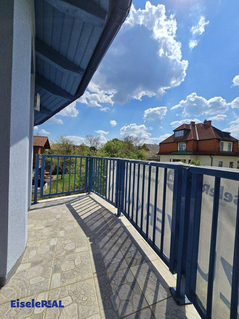 Balkon mit Fliesenboden und blauem Geländer, bietet einen sonnigen Platz im Freien.