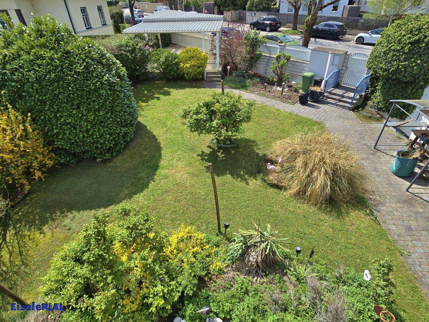 Blick von oben auf den gepflegten Garten mit Rasenflächen, Sträuchern und einem gepflasterten Weg.