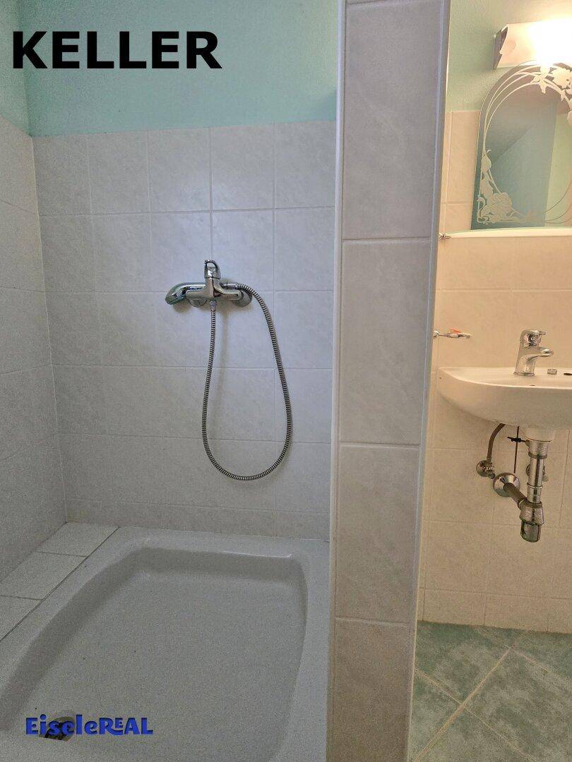 Badezimmer im Keller mit Duschwanne, Waschbecken und hellen Fliesen an den Wänden.