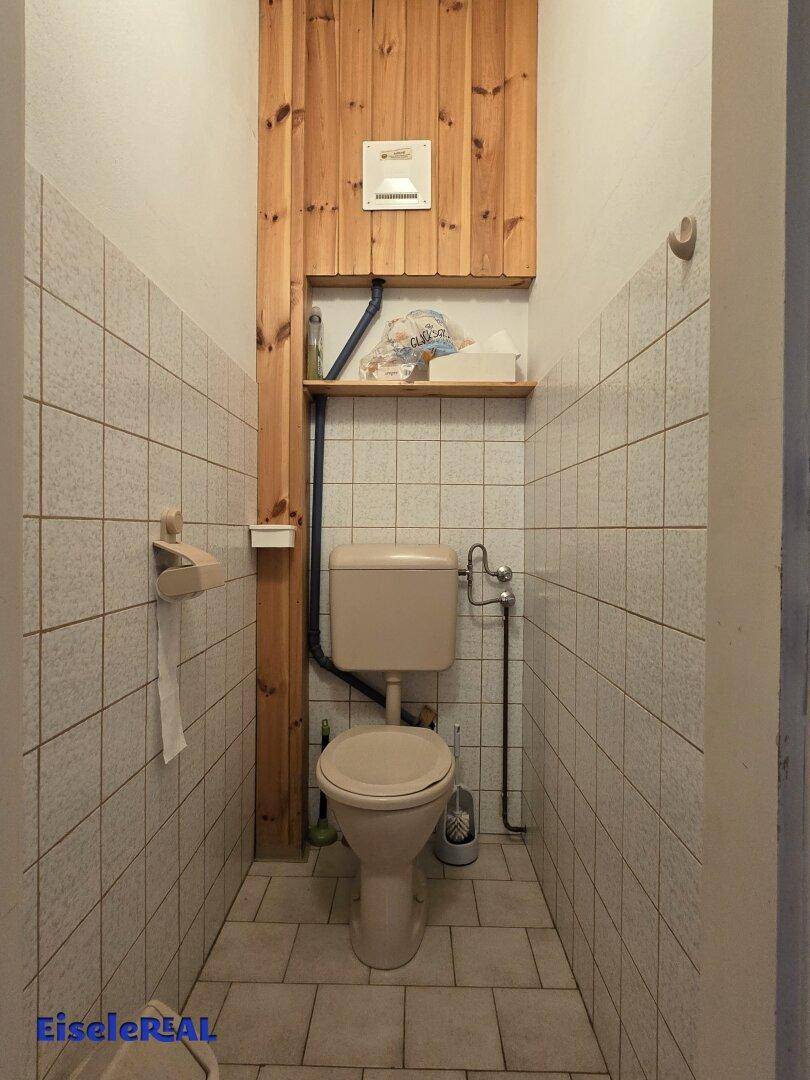 Kleines WC mit Fliesen an Wänden und Boden sowie Holzvertäfelung.