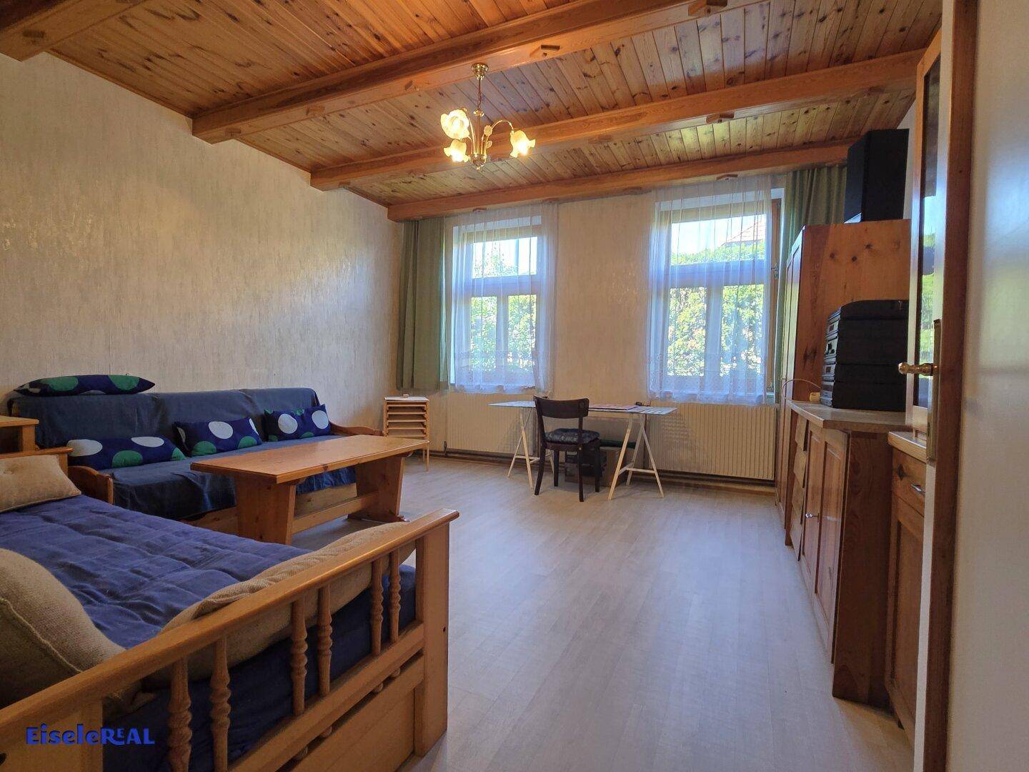 Geräumiges Wohnzimmer mit Holzbalkendecke, Sitzgelegenheiten und Blick ins Grüne.