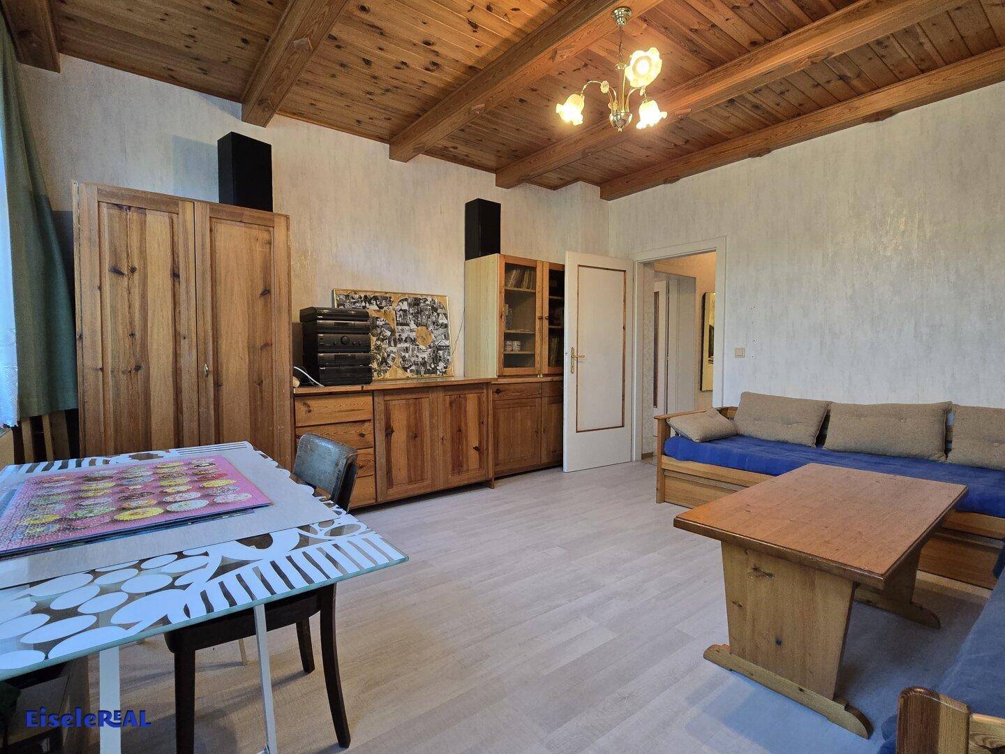 Geräumiges Wohnzimmer mit Holzbalkendecke, traditionellen Holzmöbeln und Sitzgelegenheiten.