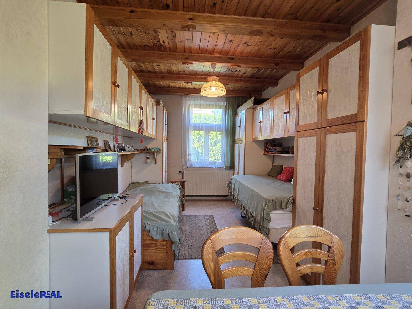 Schlafzimmer mit zwei Einzelbetten, Holzdecke und Einbauschränken.