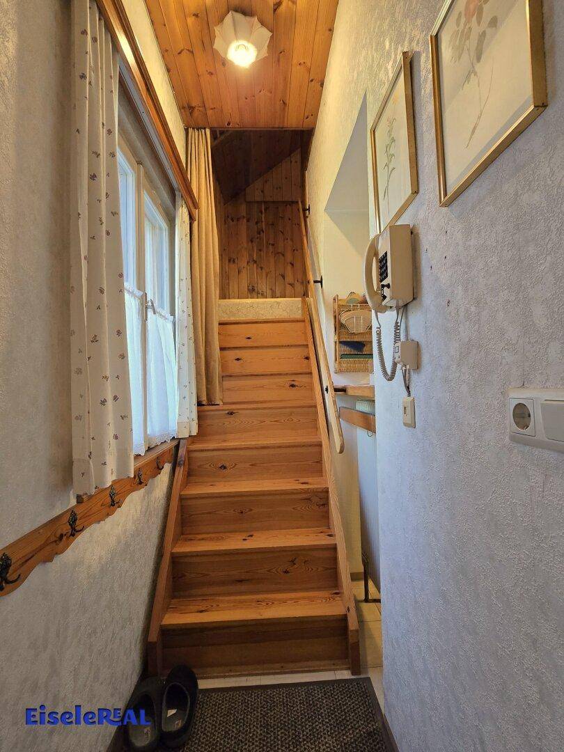 Holztreppe führt in die obere Etage, mit Fenster und traditioneller Wandgestaltung.