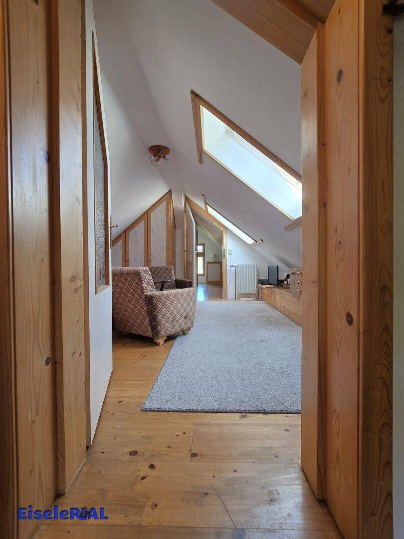 Heller Dachbodenbereich mit Holzboden, Dachfenstern und gemütlicher Sitzecke.