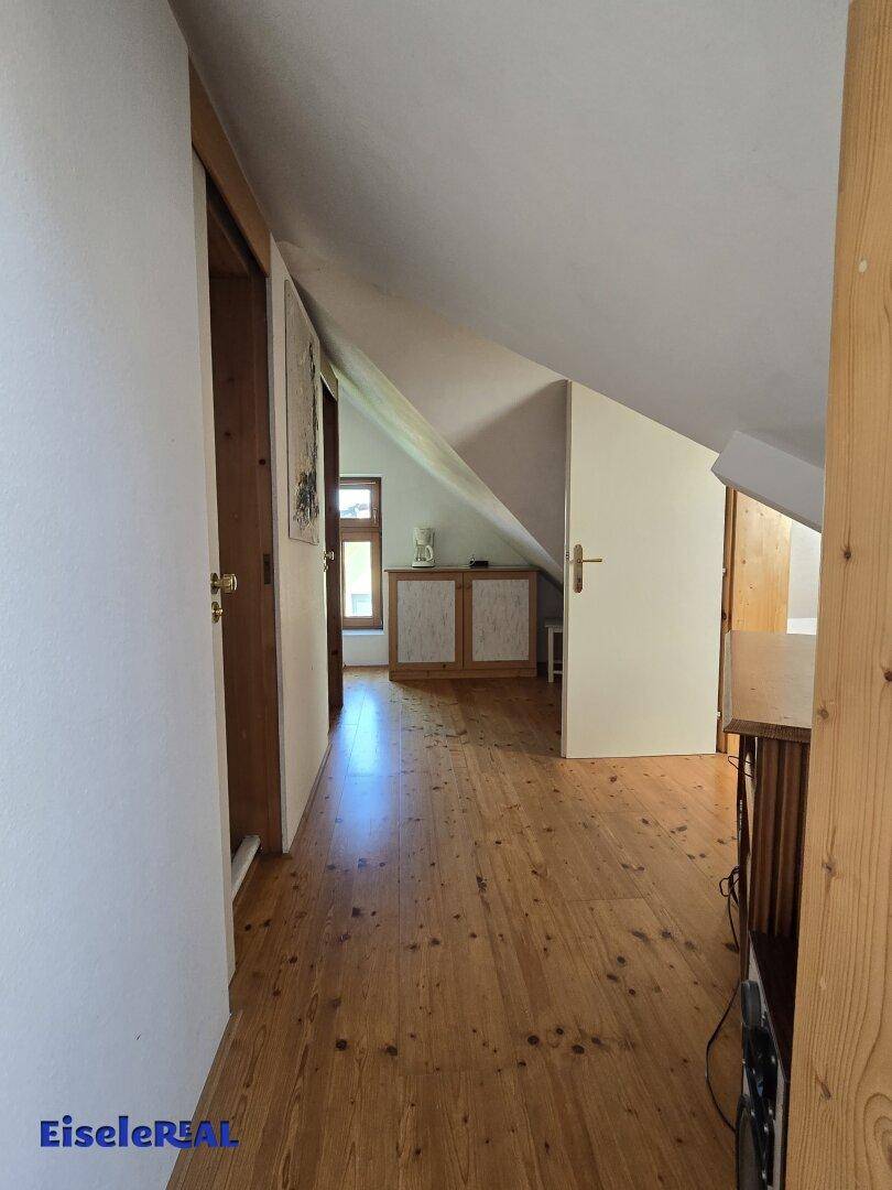 Heller Flur im Dachgeschoss mit Holzboden und schrägen Wänden, der zu weiteren Räumen führt.
