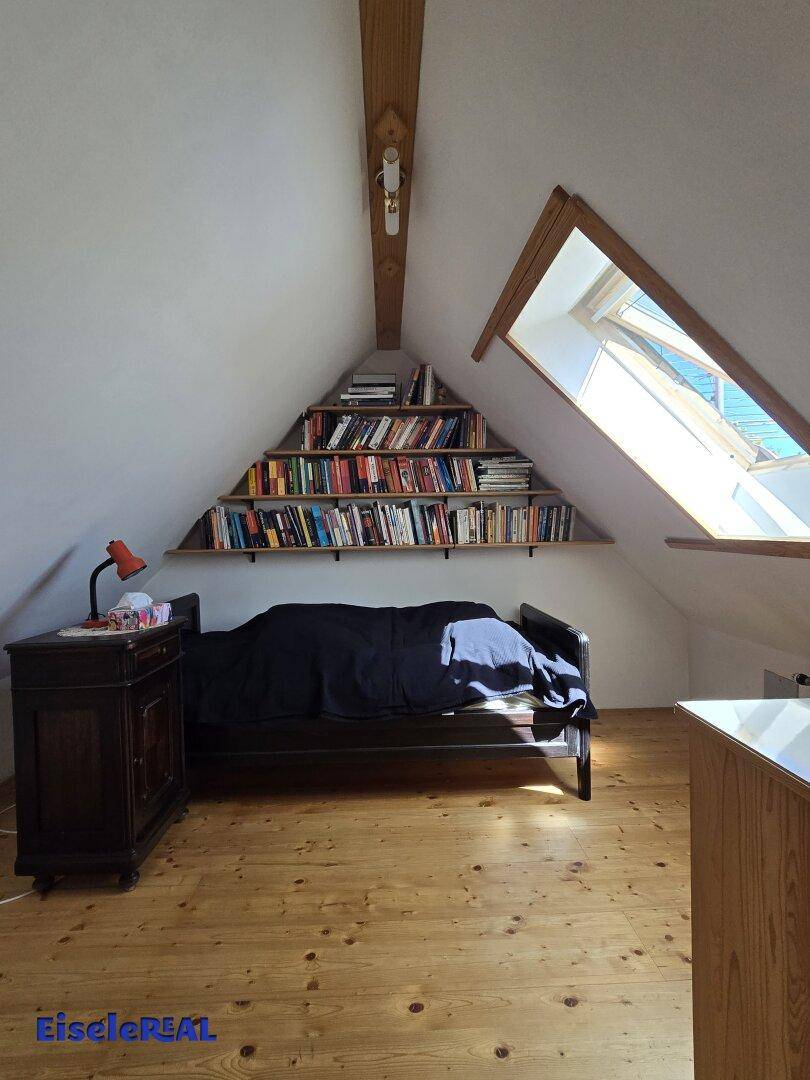 Gemütliches Schlafzimmer im Dachgeschoss mit Holzboden, Bücherregal und einem Dachfenster.