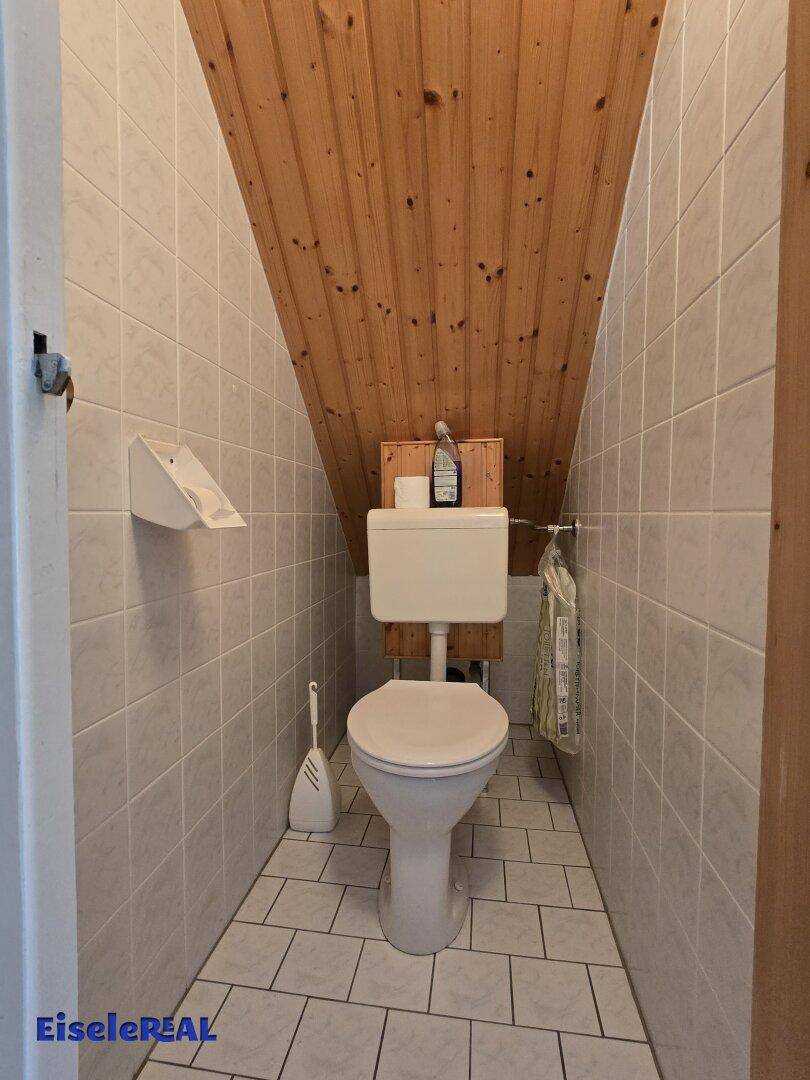 Kleines WC im Dachgeschoss mit Holzdecke, hellen Fliesen an Wänden und Boden.