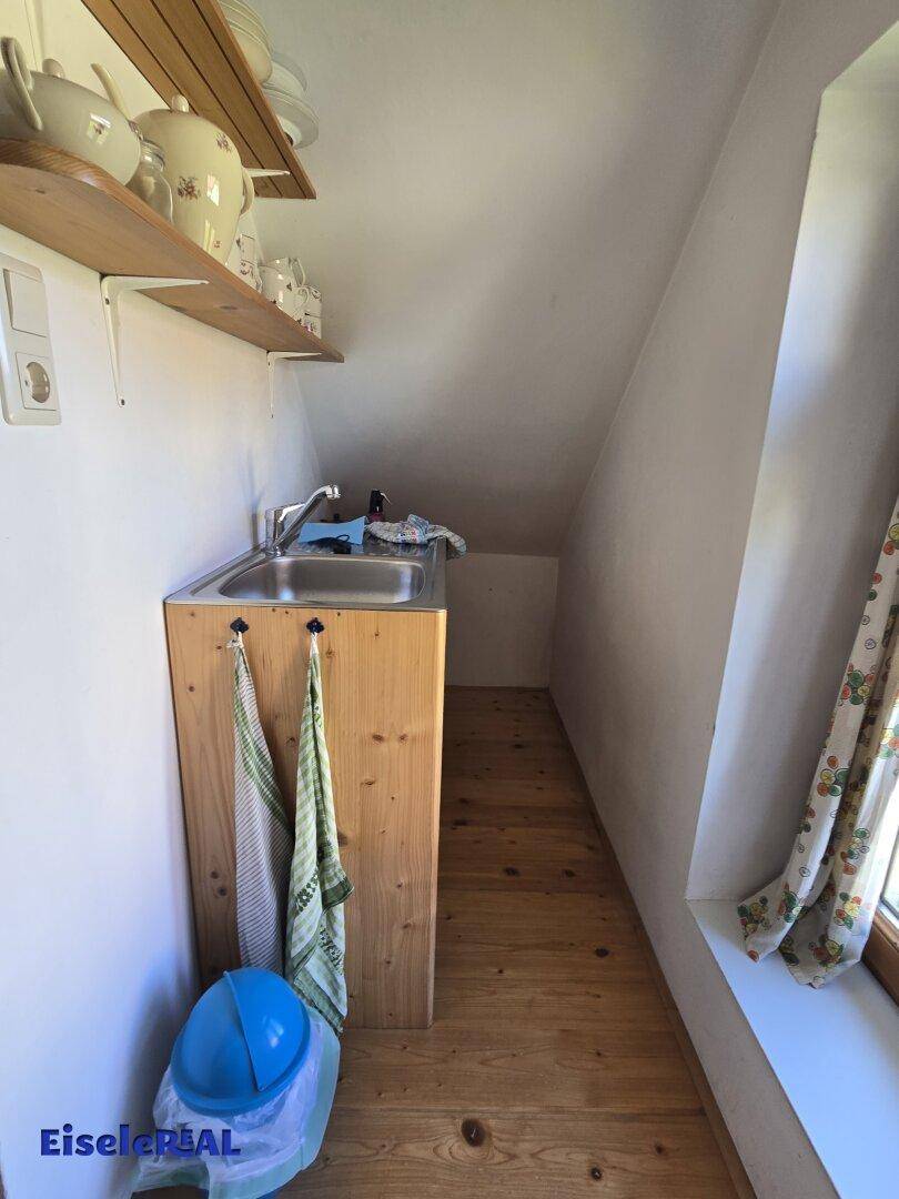 Kleiner Hauswirtschaftsraum im Dachgeschoss mit Spülbecken, Holzregalen und schrägen Wänden.