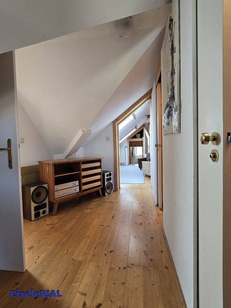 Geräumiger Flur im Dachgeschoss mit Holzboden, Schrägen und Blick in einen weiteren Raum.