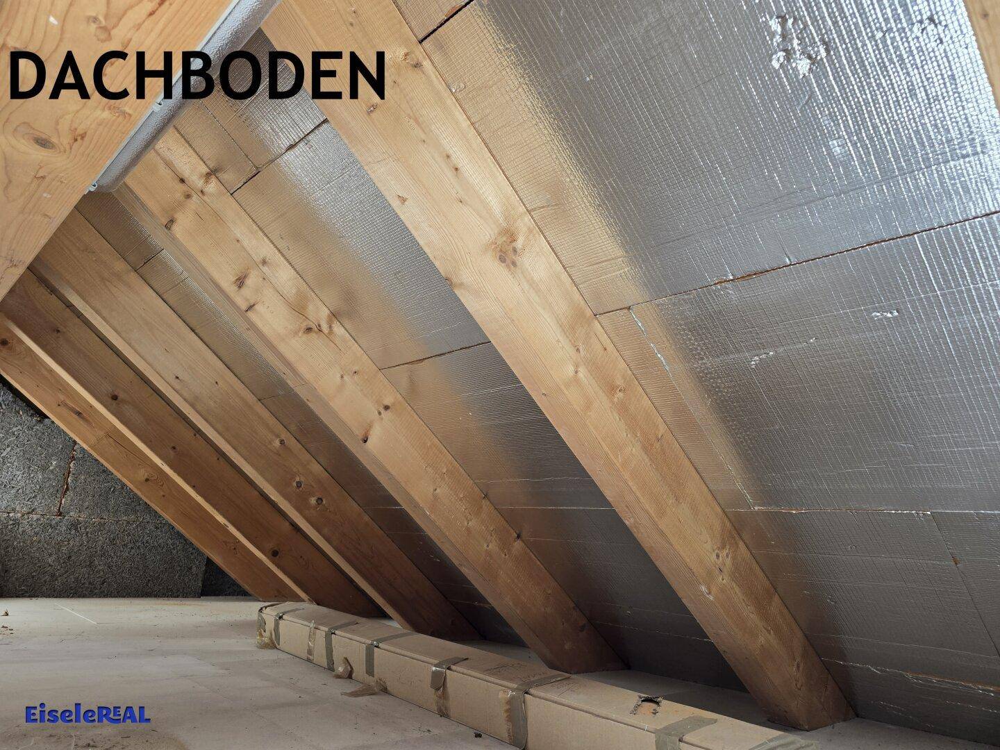 Dachbodenbereich mit markanten Holzsparren und reflektierender Isolierung an der schrägen Decke.