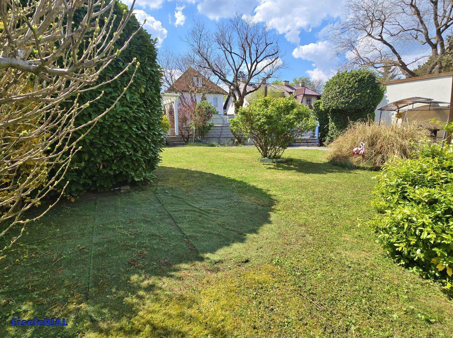 Weitläufiger Garten mit frischem Rasen und verschiedenen Pflanzen, im Hintergrund sind weitere Häuser sichtbar.