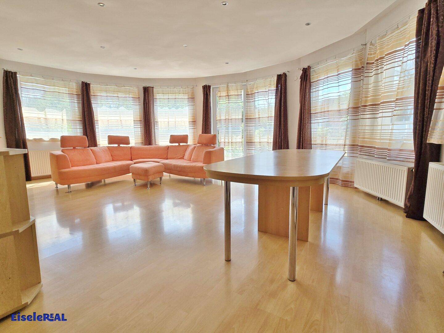 Geräumiger Wohn-Essbereich mit hellem Laminatboden, orangefarbenem Sofa und großem Esstisch.