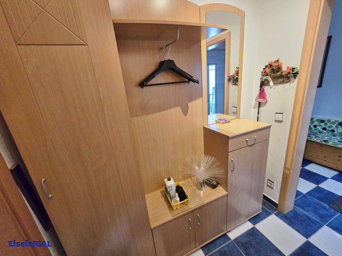 Eingangsbereich mit Holzgarderobe, Spiegel und einem markanten blau-weiß karierten Fliesenboden.
