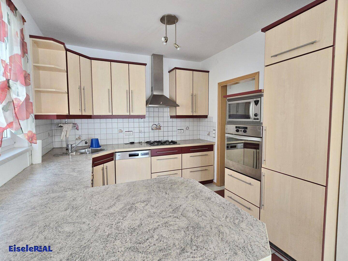 Einbauküche mit hellen Holzschränken, roten Akzenten und integrierten Geräten wie Backofen und Mikrowelle.