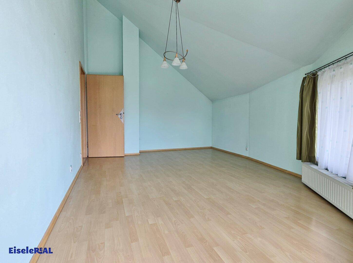 Geräumiger Raum mit hellblau gestrichenen Wänden, Laminatboden und schrägen Decken.