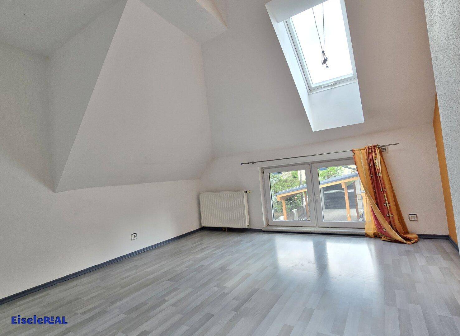 Dachzimmer mit schrägen Wänden, Dachfenster und hellem Laminatboden, bietet viel Tageslicht.