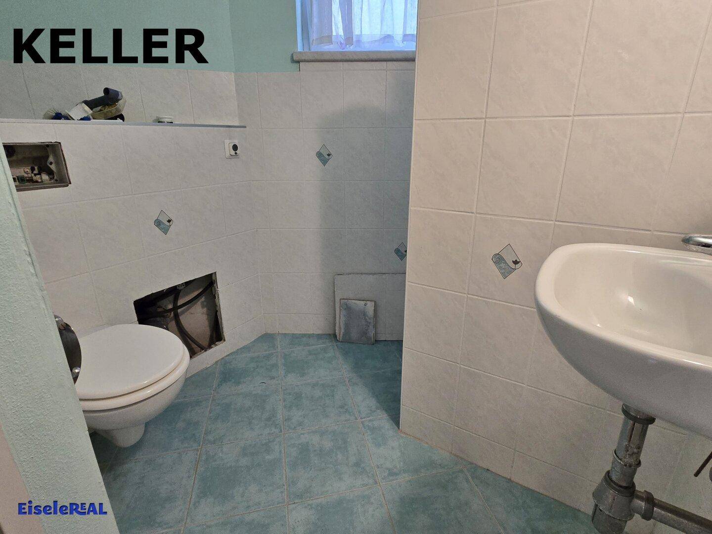 Kellerbad mit Toilette und Waschbecken, teilweise gefliest und in Renovierung.