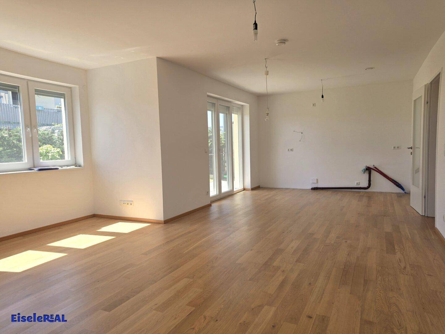 Geräumiges, helles Wohnzimmer mit Eichenparkettboden und großen Fenstern, bereit für die individuelle Einrichtung.