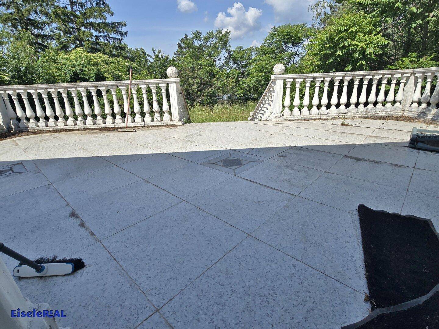 Große geflieste Terrasse mit Balustraden und Blick ins Grüne.