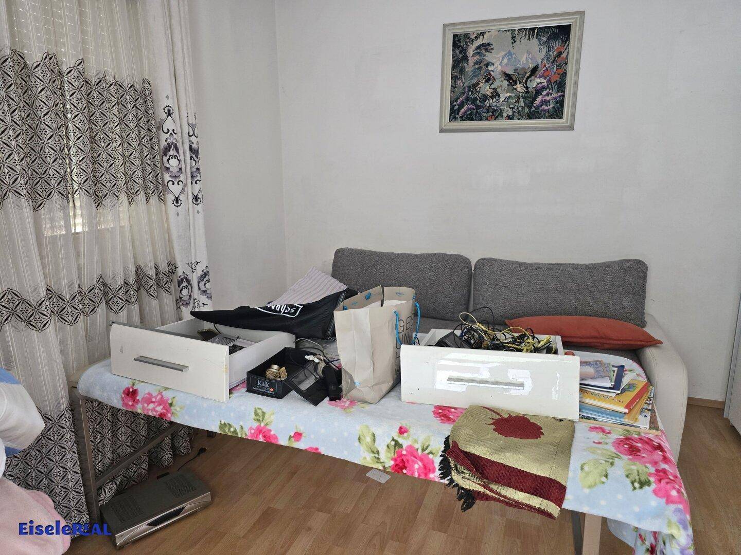 Einfaches Zimmer mit Tagesbett, floralem Überwurf und Holzfußboden.