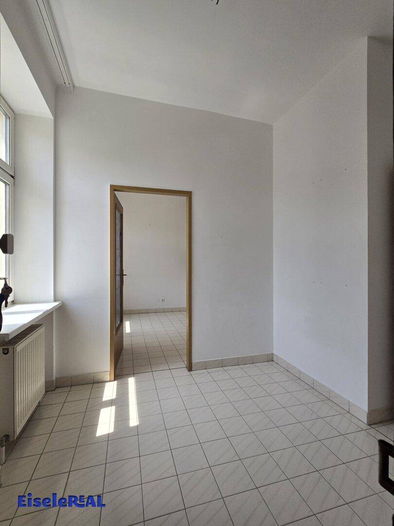 Heller Raum mit Fliesenboden und einem großen Fenster, das viel Tageslicht hereinlässt, ideal für verschiedene Nutzungen.