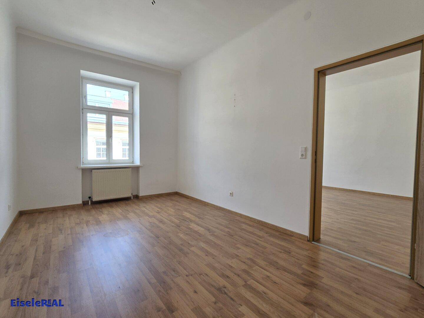 Helles Schlafzimmer mit Holzfußboden und einem großen Fenster, das den Raum mit Tageslicht versorgt.