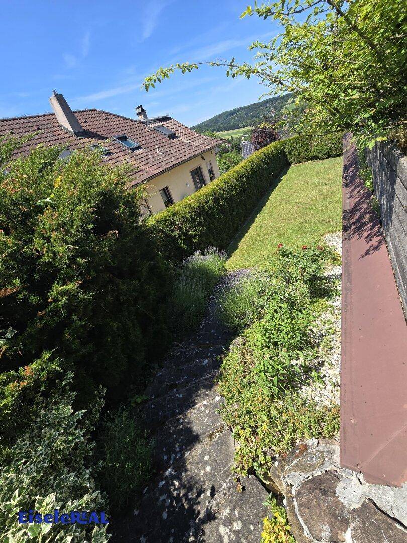 Steintreppe führt durch einen üppigen Garten mit Hecken und Blick auf das Haus und die Landschaft.