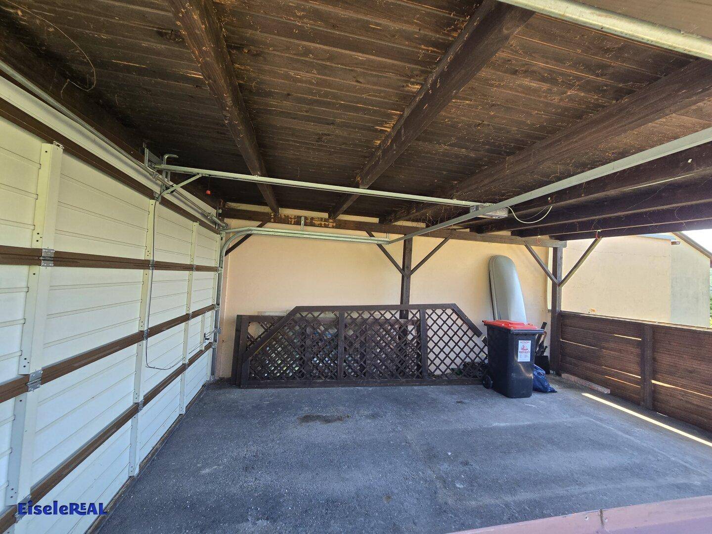 Überdachter Stellplatz oder Carport mit Holzdach und Platz für Fahrzeuge und Lagerung.